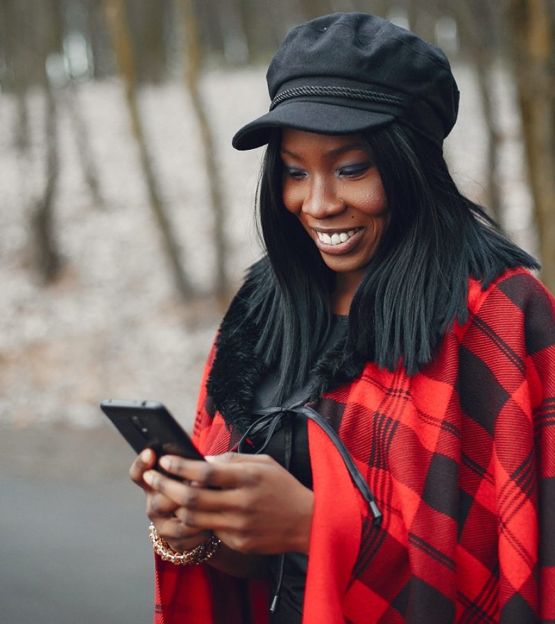 Elegant black girl in a winter park Beautiful black girl in a red shirt. Ethnic woman in a winter forest. Lady with mobile phone